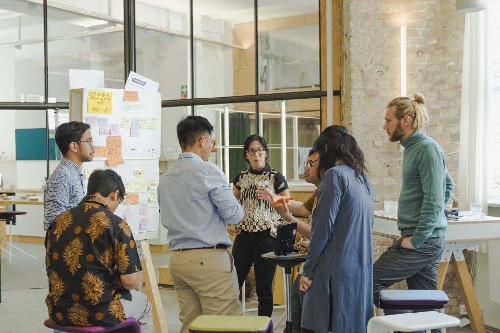 The Transisi team standing around a whiteboard of sticky notes in a bright workshop